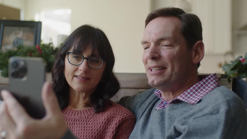 Man holds a cell phone with a woman sitting next to him and they both talk during a video chat