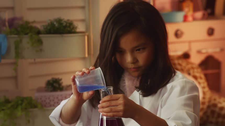 A young girl at home pours liquid in to a beaker during a science experiment