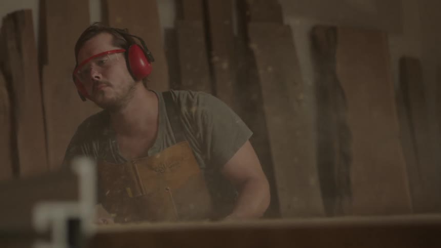 A man is working in a shop with saw dust flying from a table saw