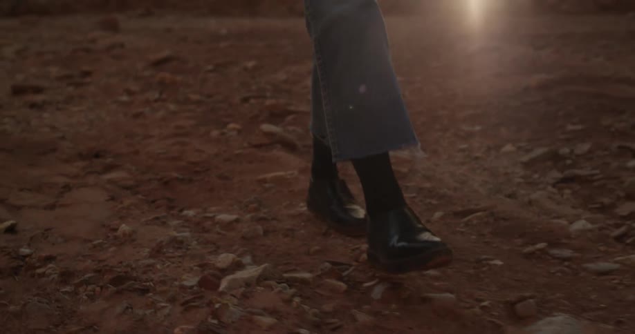 A person walks on a dirt road and kicks up dirt at dusk
