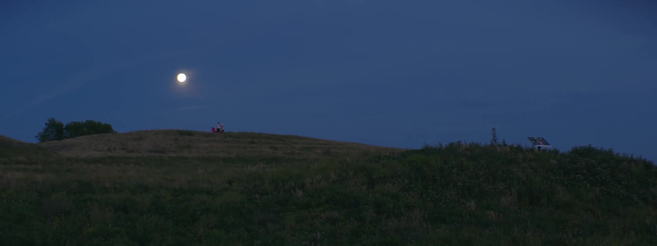 People standing on a grassy ridge with a full moon glowing brightly above