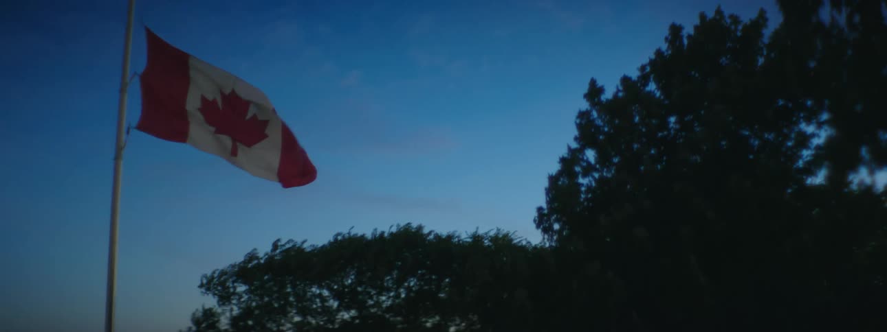 A canadian flag waves in the wind atop a flagpole at sunset