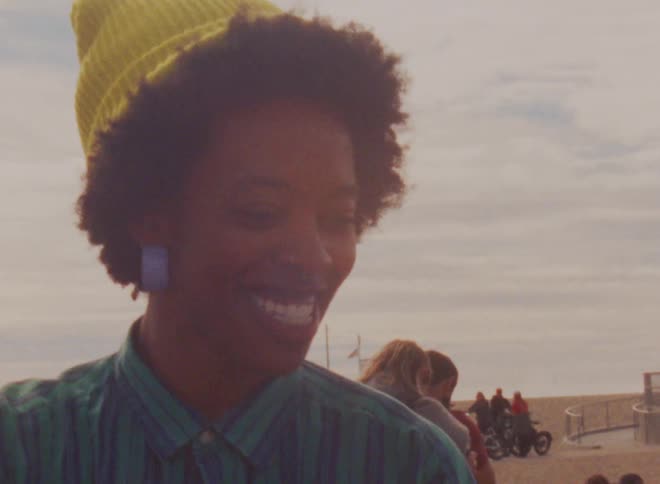 Woman with yellow wooly hat curly hair and plaid shirt smiles at her friends at social event outdoors