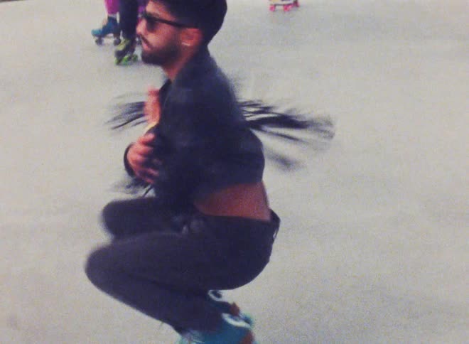 A man spins while squatting in roller skates outdoors during the day