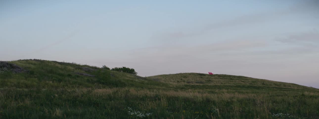 Two chairs sitting on a grassy hill under a cloudy sky