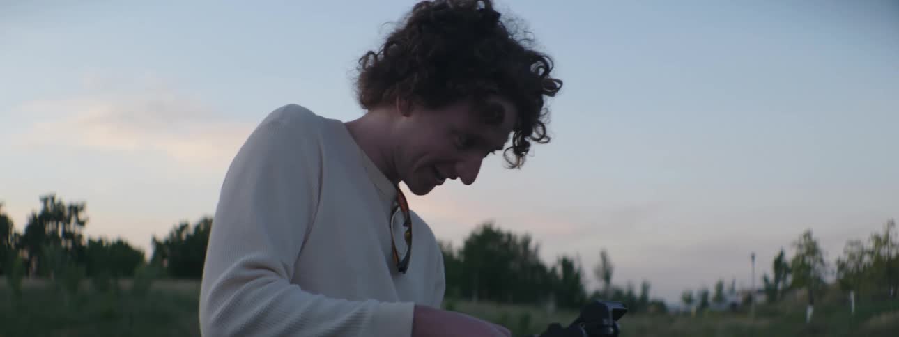 Man holds film camera while standing outdoors in field near hill