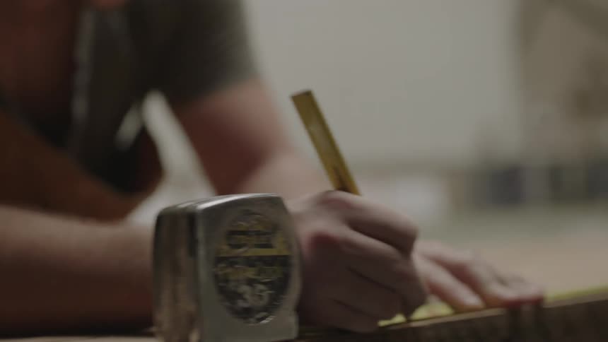 A man is using a measuring tape and using a pencil