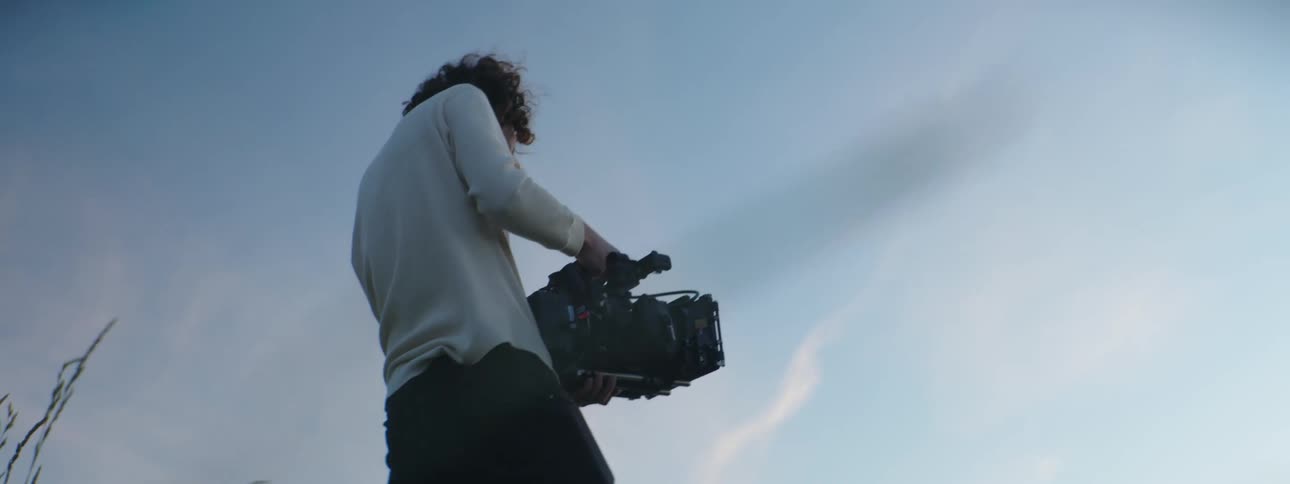 A man goes from kneeling to standing while recording video of tall grass