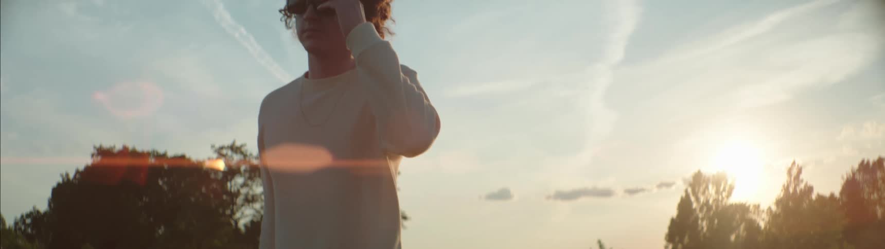 A man standing outdoors adjusts his sunglasses before walking out of frame