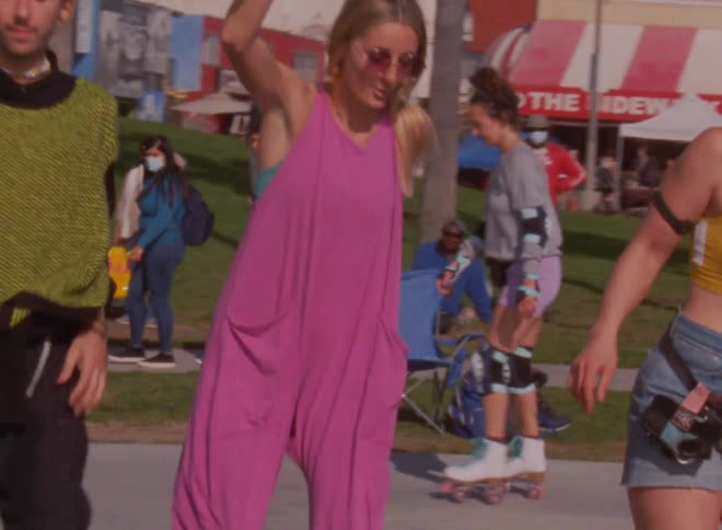 Group of young people wearing colorful clothes dance on skateboards in a park on a small town