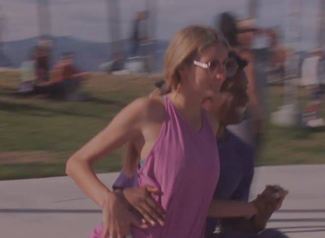 A woman leans on a mans leg as they roller skate together on venice beach