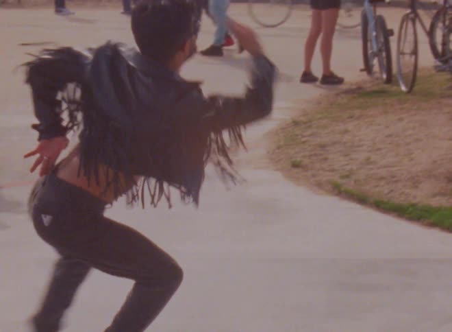A man wearing a leather jacket with fringe spins and twirls on his roller skates