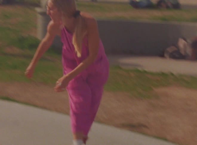 A woman does a pose while skating backwards in roller skates outdoors during the day