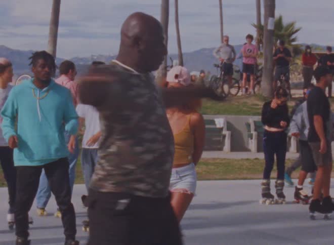 Man twirls on skates in middle of rink as others move about park with mountains in the background