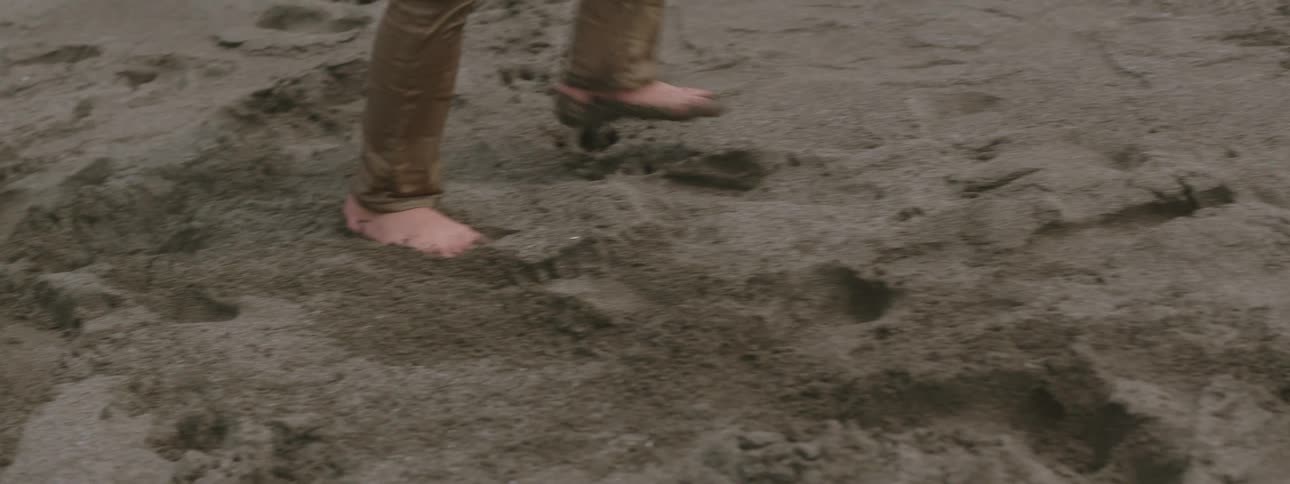 Person wearing soaked pants walks barefoot across sand
