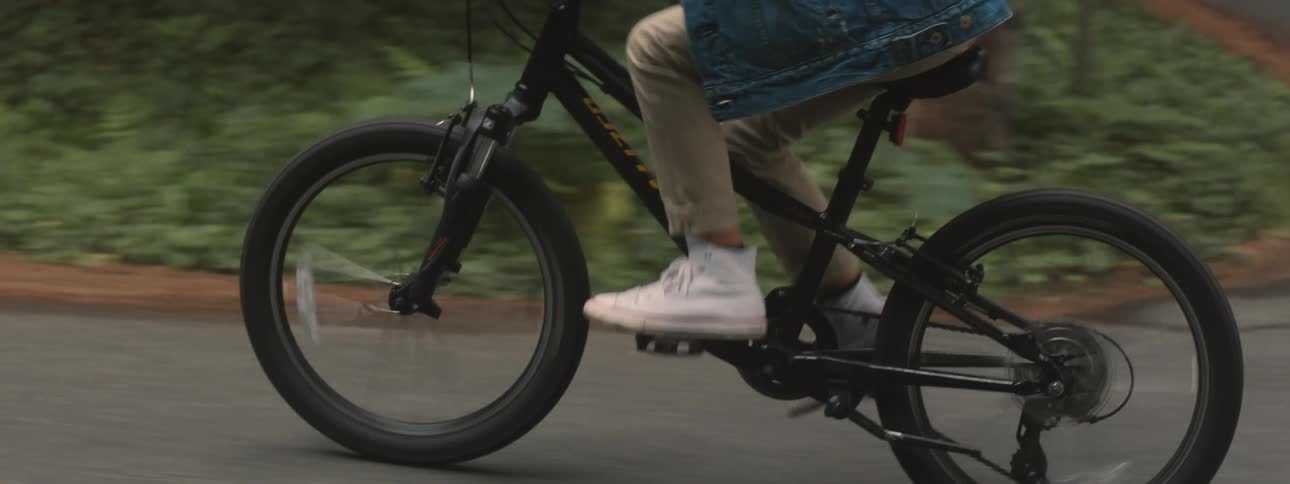 A person wearing a denim jacket rides their bicycle along a paved road