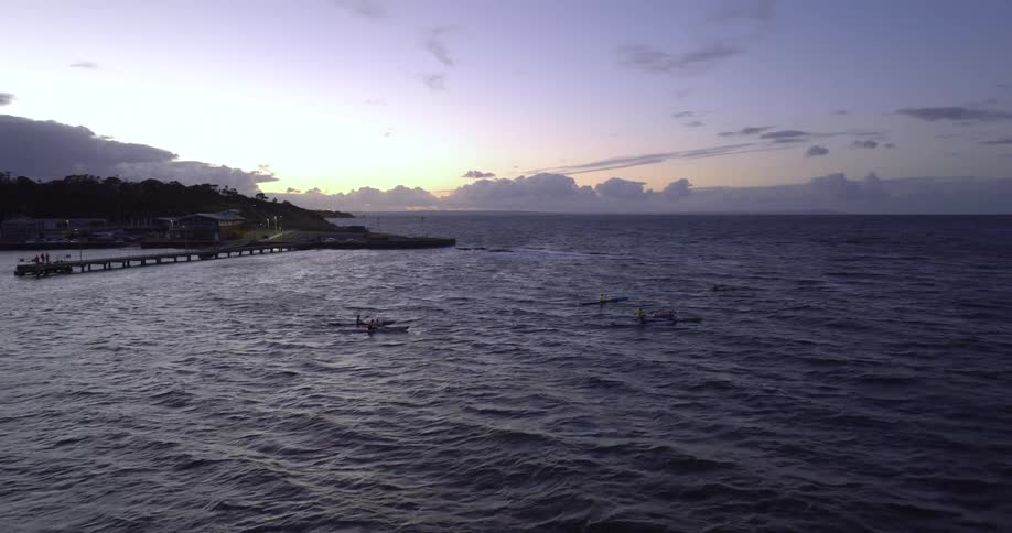 People paddle out to sea as sky on horizon brightens over town