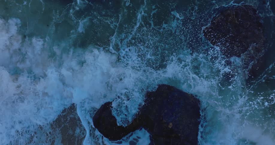 Powerful waves crash against a large rock that is protruding from the ocean surface