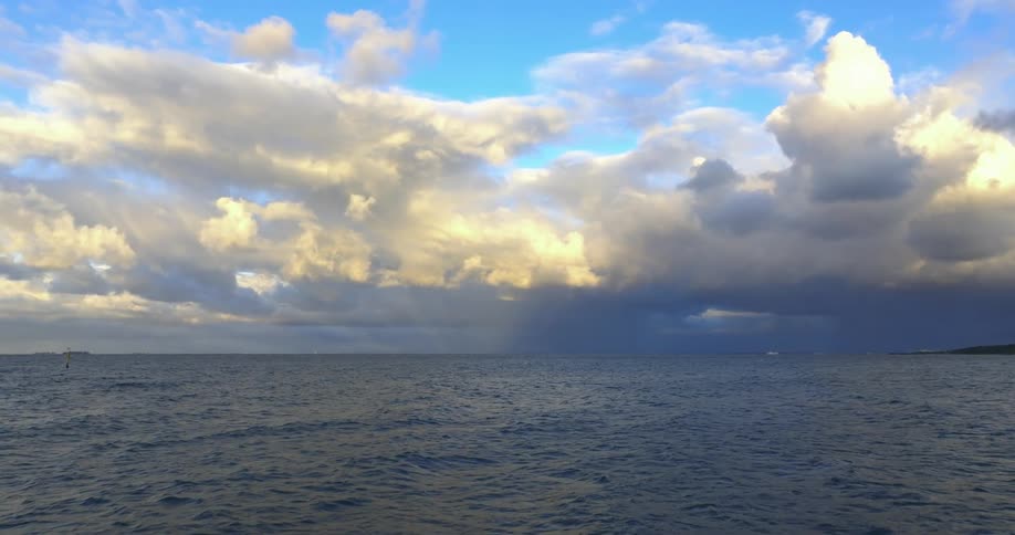 Waves roll toward storm on the horizon near the distant green shore
