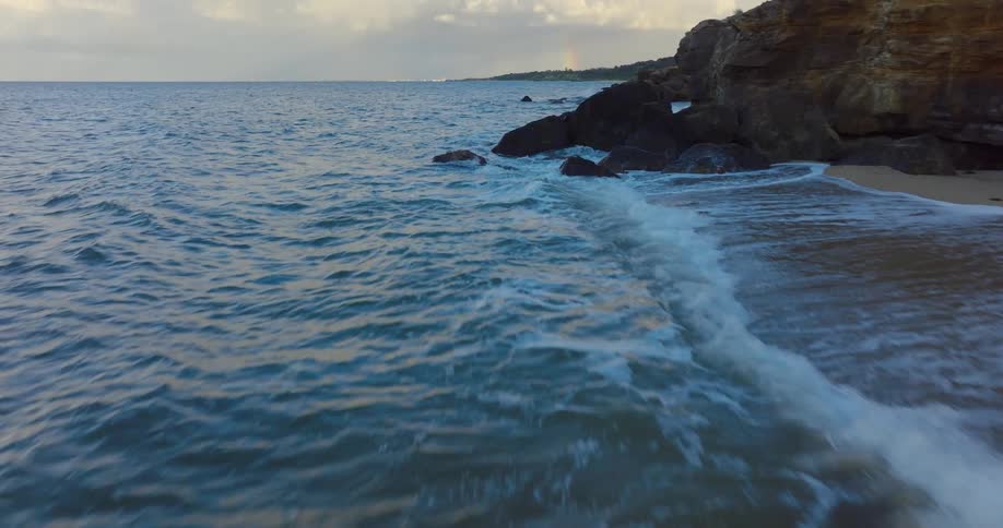 Waves roll in over a beach and rocks along the coastline under a cloudy sky