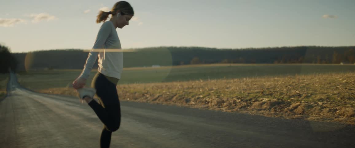 A woman stretches her legs while standing on a rural road near a field