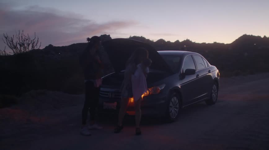 Family standing near a stalled car parked on a rural road at sunset waiting for assistance
