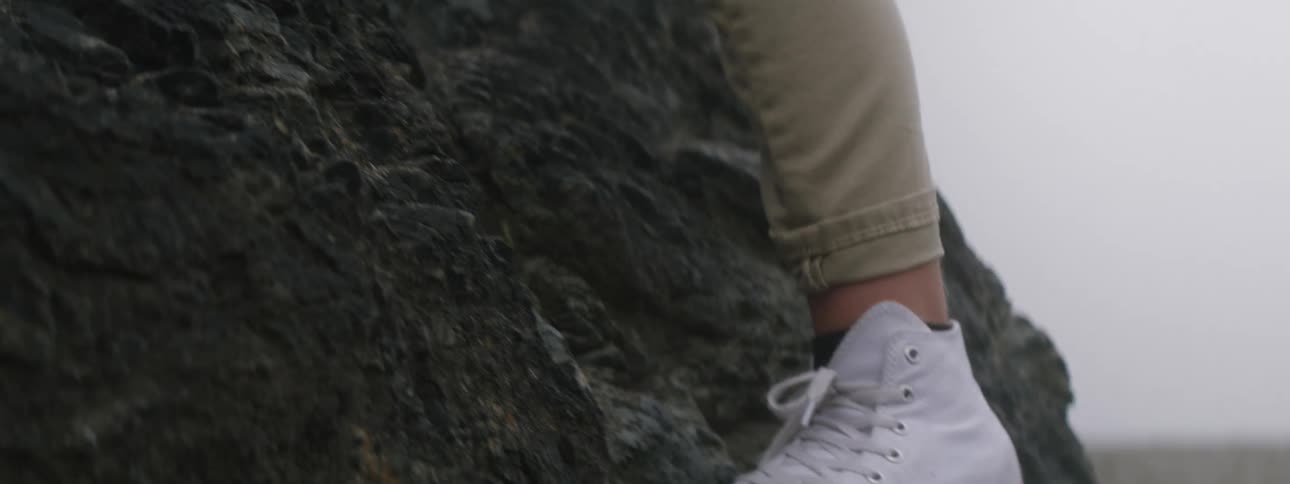 A person wearing white shoes carefully climbs up a rocky cliff