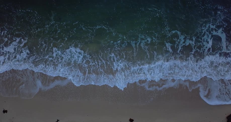 Waves crash onto beach foaming up as they move on the sand