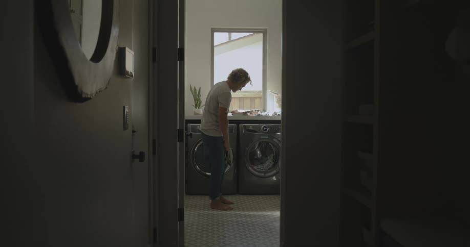 A man folds laundry and stacks it on his washer and dryer