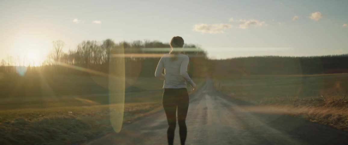 Woman jogs along countryside road as sun shines near the horizon