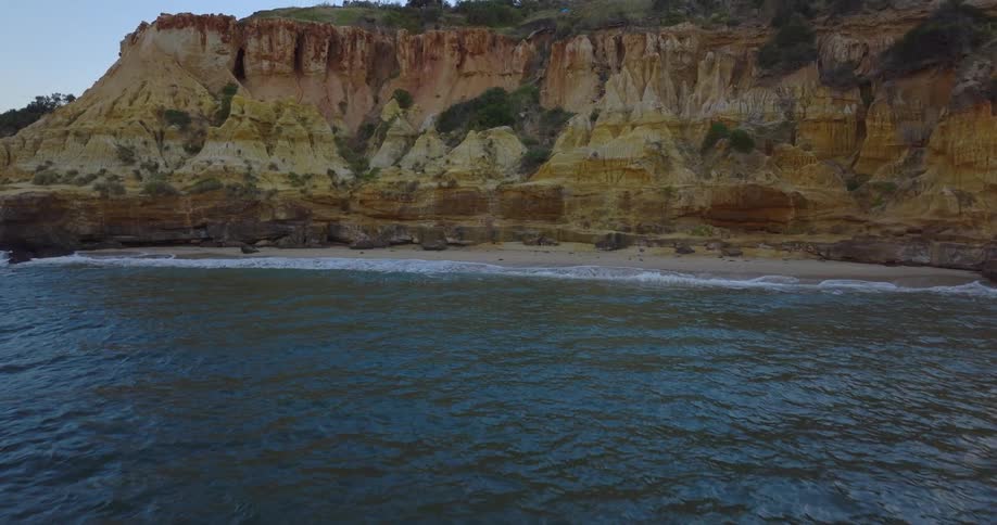 Waves flow toward beach and striated cliff