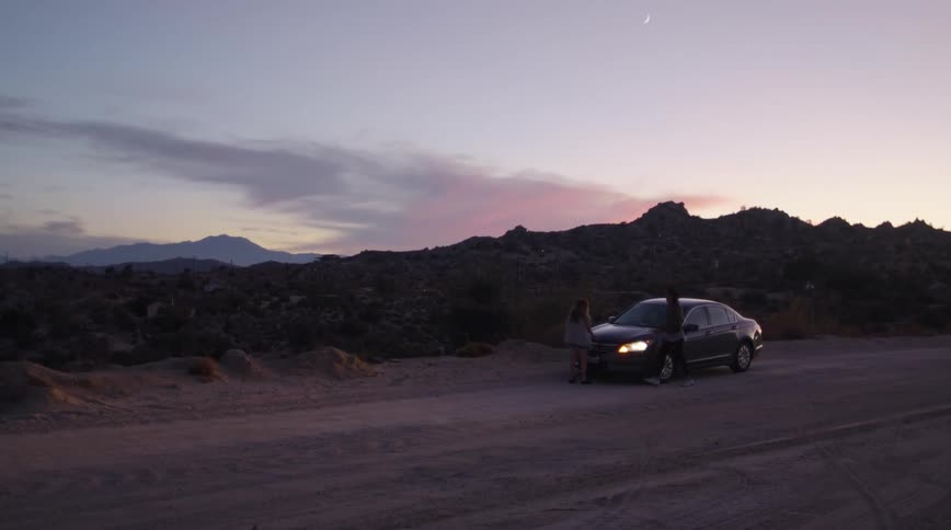 A man and woman walk to their broke down vehicle