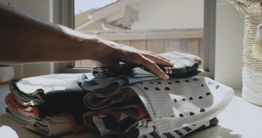 Man places folded clothes over a shelf near a window under the bright sunlight