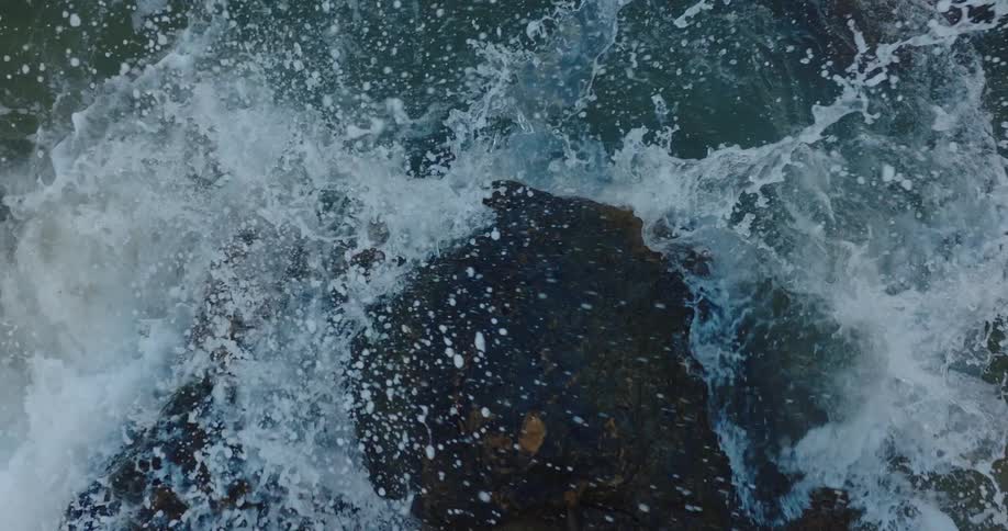 Ocean waves crash into a large rock on the shore during the day