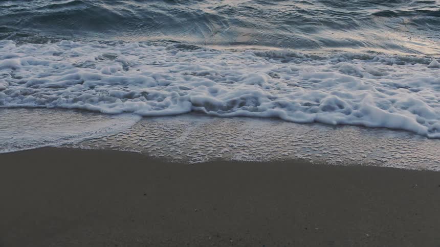 Waves foam up as they crash on smooth sand on beach