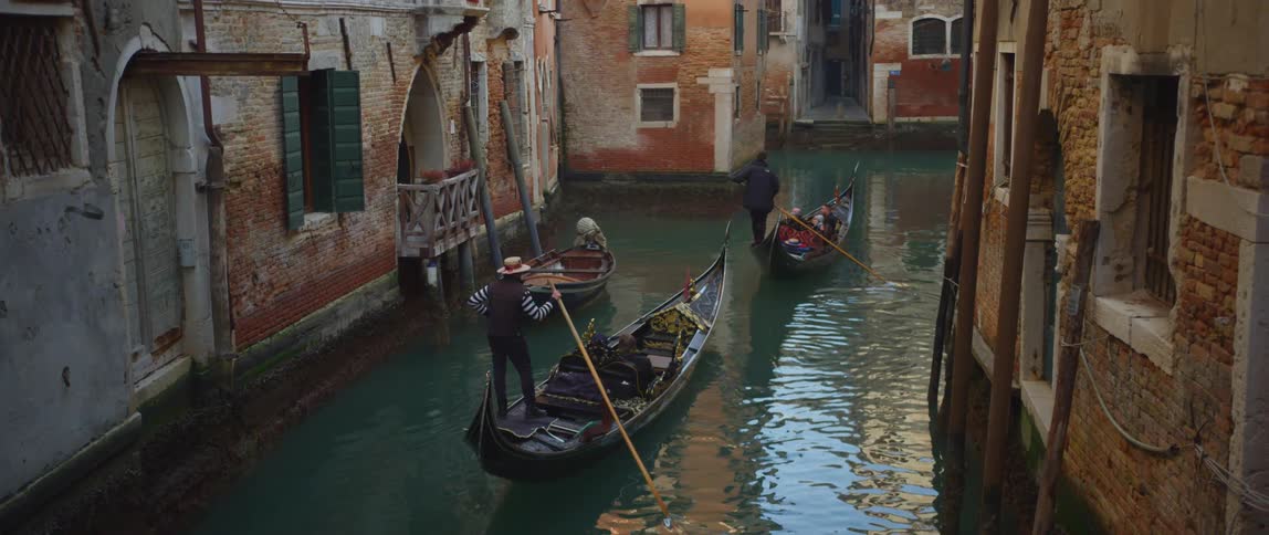 Gondoliers ferry passengers down a canal with historic buildings in Venice, italy