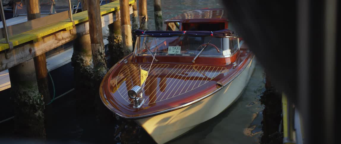 A docked water taxi boat with highly polished deck bobs in the water in a canal in Venice, Italy
