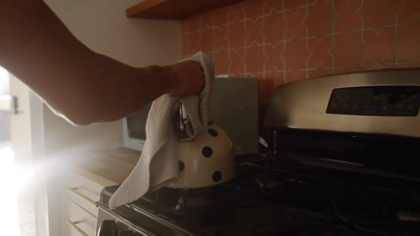 A person lifts the kettle from the stove