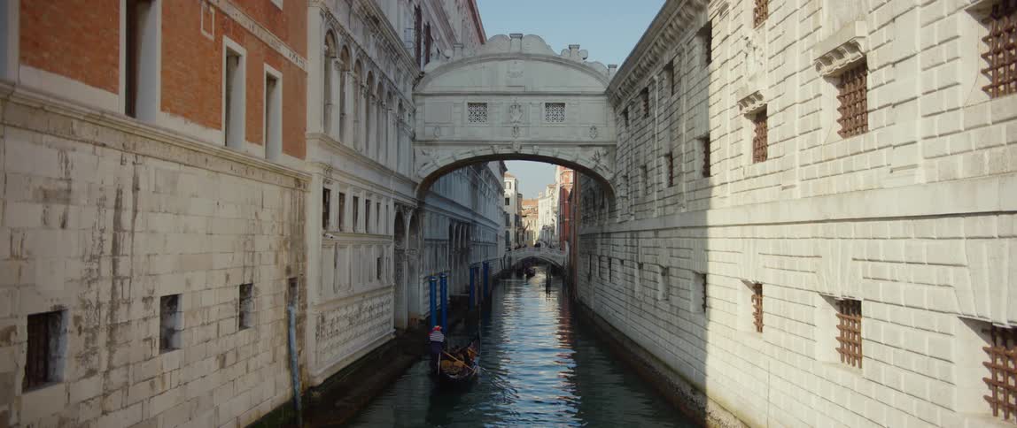 People riding in a gondola on Rio di Palazzo under the Bridge of Sighs which connects the new prison to the Doge's Palace.