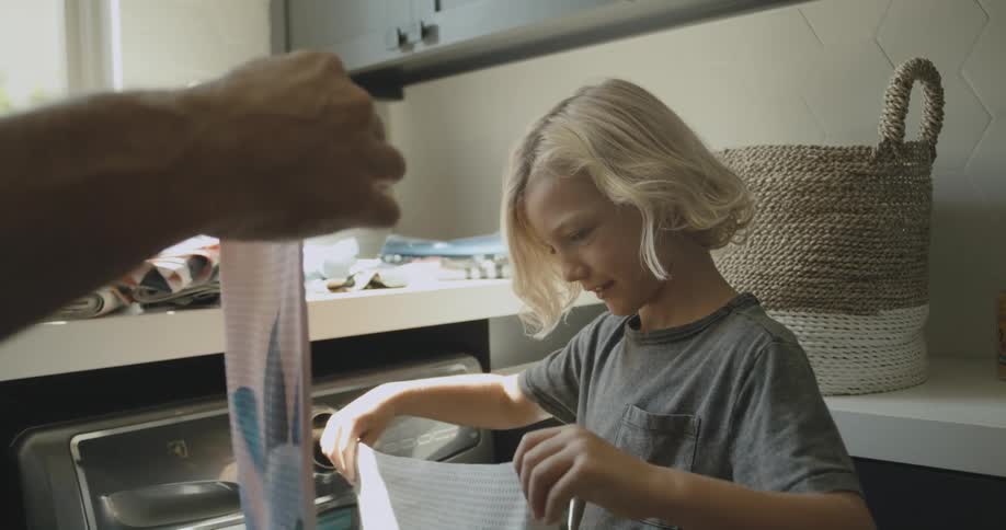 Dad holding up a towel in the laundry room showing his son how to fold