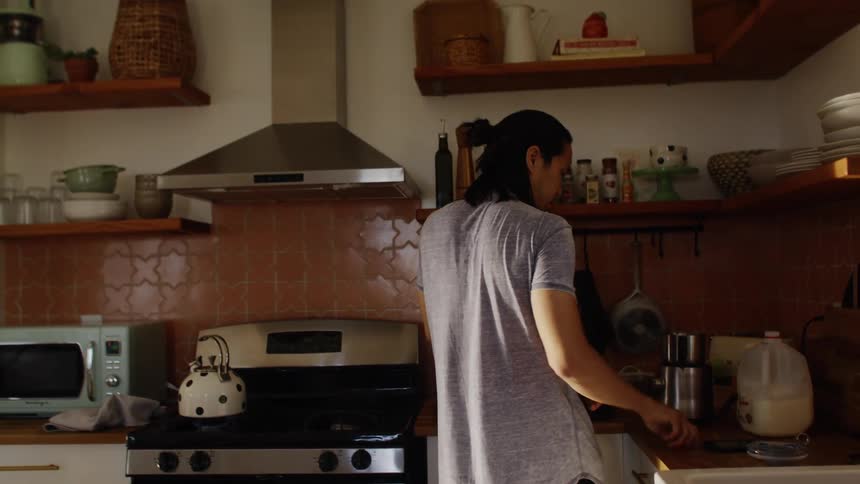 Father works with milk and counter top appliance in kitchen while holding child