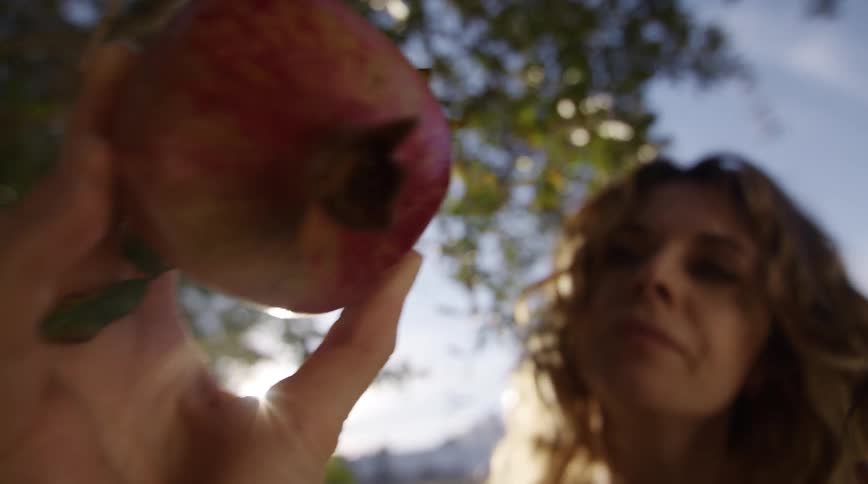 A mother holding a pomegranate and baby outside on a sunny summer day