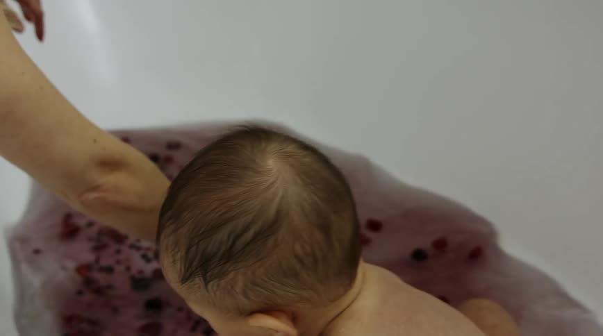 Mom swirls the berries in the bath water while baby sits in the tub picking up and eating berries