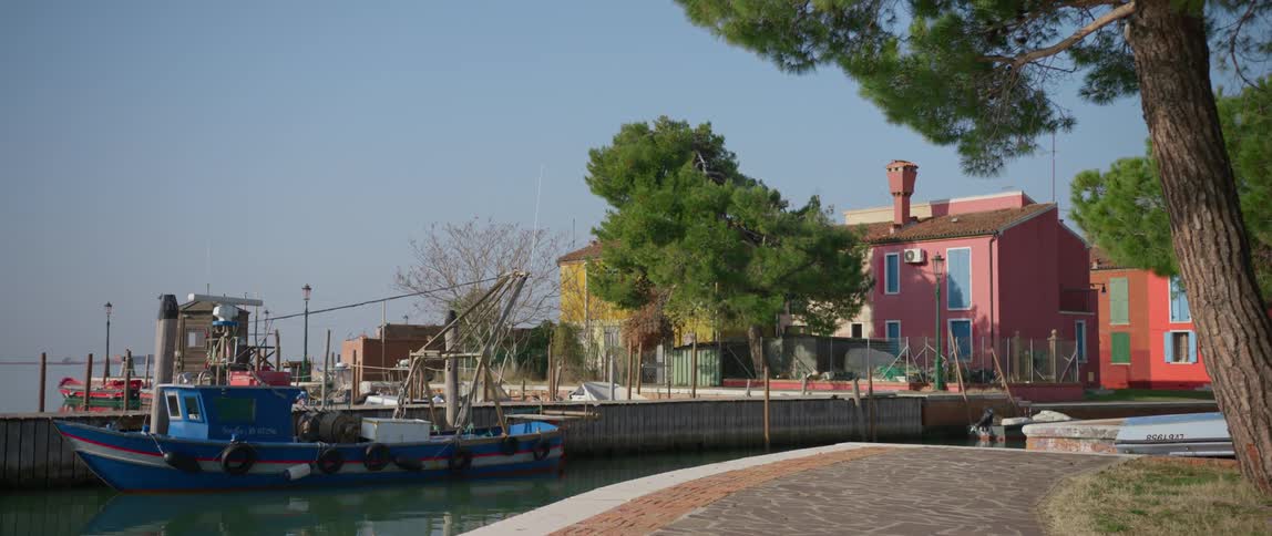 A boat is docked in a canal near colorful homes on Burano Island, Venice, Italy