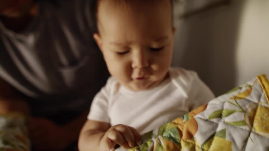 A baby plays with an oven mitt and his father leans down and kisses him