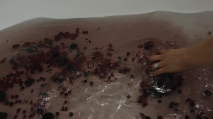 A person stirs a bathtub filled with water and berries with their hand