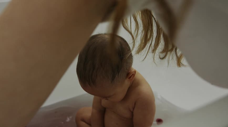 A woman swirls her arm in bath water while bathing her baby
