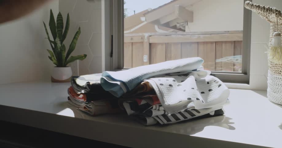 A child and an adult stack folded towels on a table indoors during the day