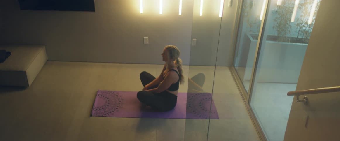 A woman practices yoga on a yoga mat indoors during the day