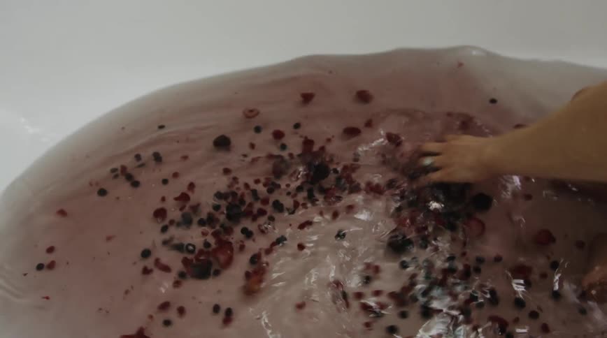 Woman stirs water full of fruit in tub as child sits in water